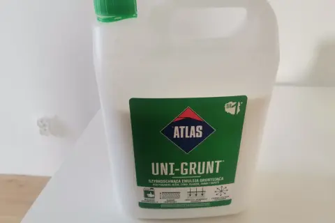 Biały kanister z zieloną nakrętką, zawierający emulsję gruntującą Atlas Uni-Grunt. Szybkoschnący produkt, idealny do przygotowania podłoży przed malowaniem, klejeniem czy tynkowaniem.