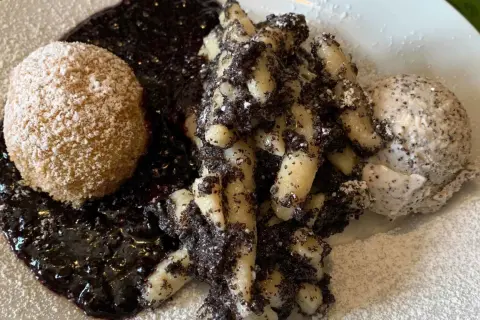 Gedrehte Nudeln mit Mohn, eine Kugel und Beerensoße, bestäubt mit Puderzucker.