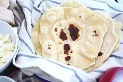 Färska tortillabröd, perfekta för ditt nästa tortilla recept. Bredvid syns skålar med tillbehör som ost och lök.