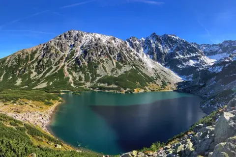 Piękne Tatry dla początkujących: Morskie Oko otoczone zielenią i ośnieżonymi szczytami. Tłumy turystów podziwiają widok.