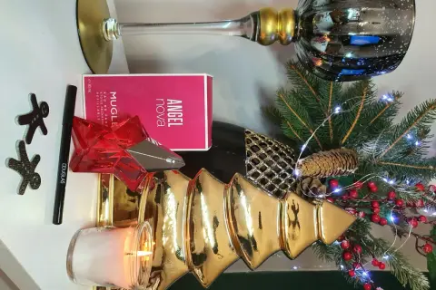 Świąteczna kompozycja z perfumami Angel Nova Mugler 50 ml, świecą, choinką i ozdobami.