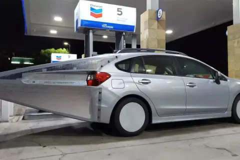 Silverbil med en stor, silverfärgad aerodynamisk förlängning bak. En uppfinning för att spara bensin vid en Chevron-mack.