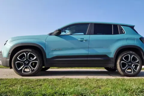 Turkusowy suv premium Jeep Avenger z czarnymi akcentami i felgami stoi na tle błękitnego nieba.