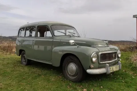 Grön Volvo P210 parkerad på en gräsmatta. Bilen har en klassisk design och ser ut att vara i gott skick.