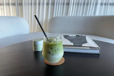 Un verre de lait matcha glacé, parfait pour profiter des bienfaits du matcha. Une petite boîte de matcha est à côté.