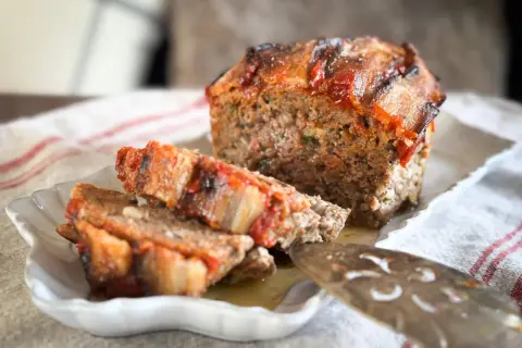 Un délicieux pain de viande, garni de tomates et de lardons, est servi sur une assiette blanche.