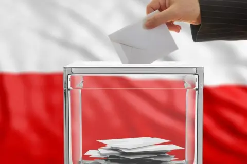 Dłoń wrzuca kartę do urny wyborczej. Polska flaga w tle symbolizuje kraj, od którego można głosować.