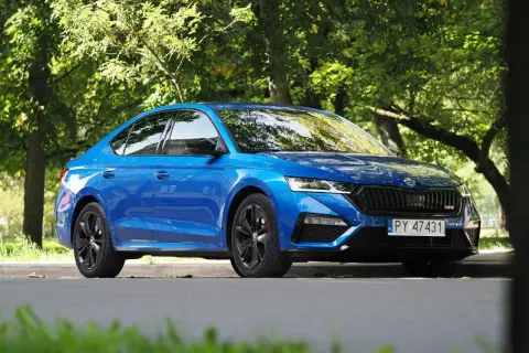 Błękitna Skoda Octavia RS 2025 z czarnymi felgami, zaparkowana wśród zieleni.