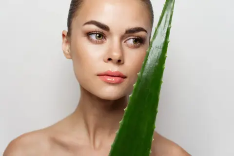 Mujer con piel radiante sostiene una hoja de aloe vera, demostrando que se puede usar aloe vera directamente de la planta para un cuidado natural.