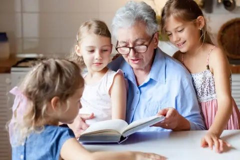 Babcia czyta książkę trzem wnuczkom przy stole.
