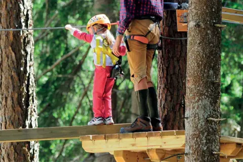 Bambina con casco giallo e adulto su passerella in un parco avventura Marche.