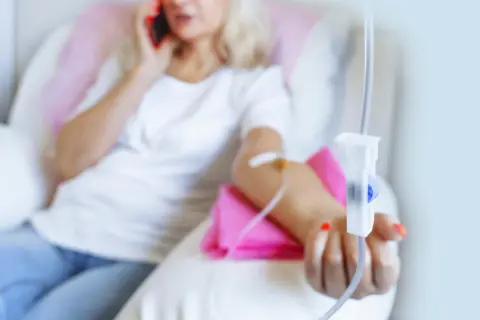 Frau erhält Infusion, während sie telefoniert. Thema: Brustkrebs HER2 und Lebenserwartung.