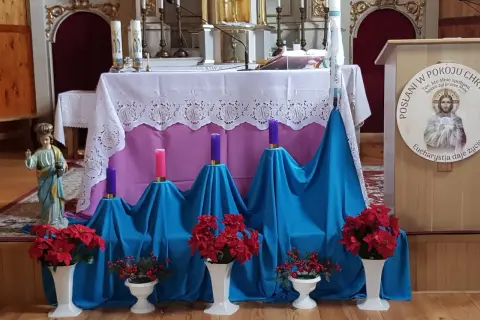 Ołtarz kościelny udekorowany na adwent: świece, kwiaty i figurka.