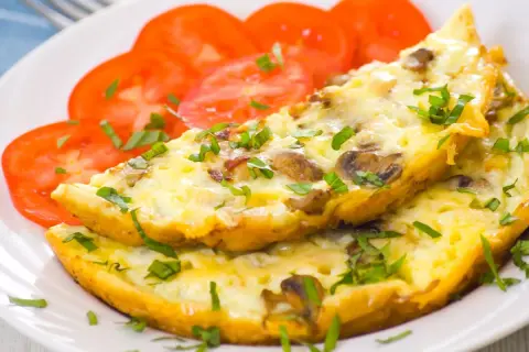 Puszysty omlet z pieczarkami i natką pietruszki, podany z plastrami pomidora. Idealne śniadanie.