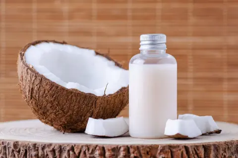 Aceite de coco en botella junto a coco partido. Considera las contraindicaciones del aceite de coco antes de usarlo.