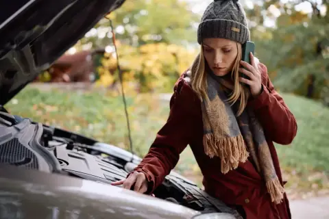 Kobieta z telefonem przy uchu sprawdza silnik auta, zastanawiając się, dlaczego nie można holować automatu.