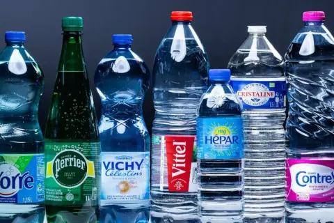 Une rangée de bouteilles d'eau minérale, dont Perrier, Vittel et Contrex, évoque le scandale de l'eau en bouteille.