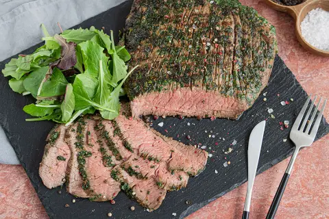 Saftiges Flank Steak, mariniert und perfekt gegrillt, mit frischem Salat und Gewürzen auf einem Schieferbrett serviert.