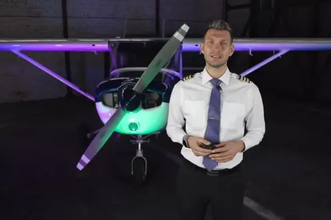 Mężczyzna w stroju pilota przed samolotem, oświetlonym kolorowymi światłami. Chcesz wiedzieć, jak zostać pilotem?