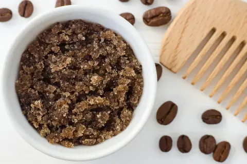 Domowy peeling do skóry głowy z kawy w białej miseczce, obok drewniany grzebień i ziarna kawy.
