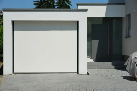 Moderne grenzbebauung mit weißer Garagentür und dunkler Eingangstür. Gepflasterte Einfahrt.