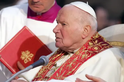 Papież Jan Paweł II podczas modlitwy do Ducha Świętego o uzdrowienie. W rękach trzyma dokument i czerwoną księgę.