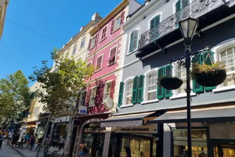 Edificios coloridos y tiendas en la Gibraltar altstadt, con gente paseando bajo un cielo azul brillante.