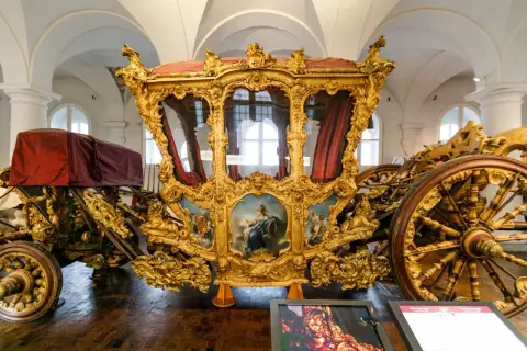 Prunkvolle Kutsche im Marstall Museum, vergoldet und mit Gemälden verziert, ein Zeugnis vergangener Pracht.