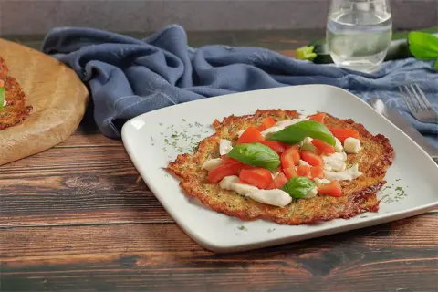 Eine köstliche low carb pizza mit Tomaten, Mozzarella und Basilikum auf einem weißen Teller.