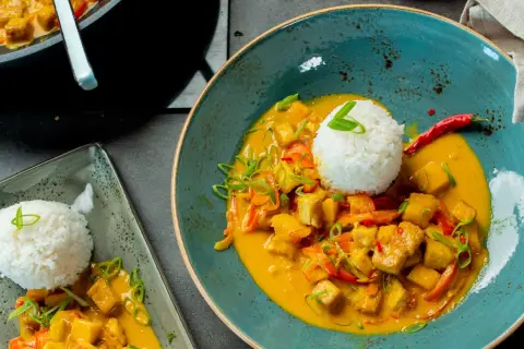 Ein köstlicher Thai Curry mit Tofu, Gemüse und Reis, garniert mit Frühlingszwiebeln und Chili.