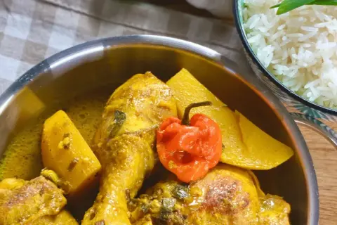 Un plat de poulet au curry, parfumé par l'épice colombo, avec des morceaux de patate douce et un piment rouge. Servi avec du riz blanc.