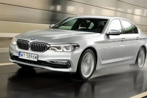 Srebrne BMW 520d xDrive pędzi po mokrej drodze w tunelu, rozpryskując wodę.