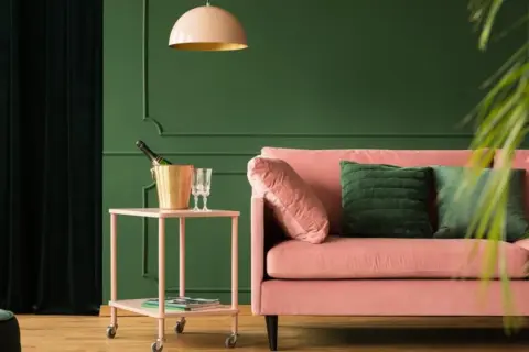 Różowa kanapa i złoty kubełek na szampana na stoliku. Wnętrze w odcieniach zieleni, gdzie kolory metali dodają elegancji.