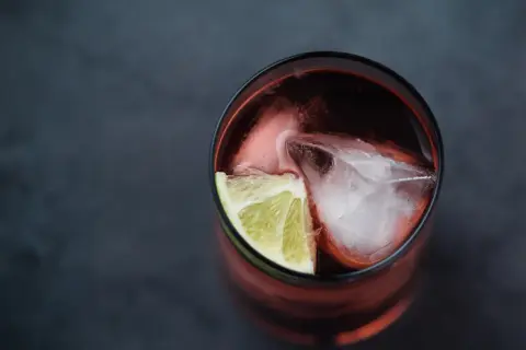 Szklanka z ciemnym napojem, lodem i plasterkiem limonki. Idealny drink z Asbach Uralt, by poczuć smak lata.