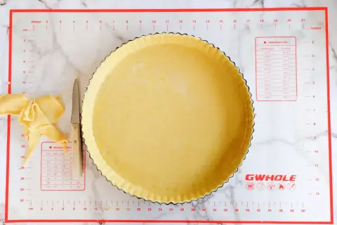 Préparation d'une conservation pâte brisée maison dans un moule à tarte, avec des chutes de pâte et un couteau.