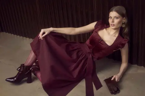 Ein elegantes Dirndl mit schwarzer Strumpfhose und auffälligen Stiefeln. Die Frau liegt lässig auf dem Boden.
