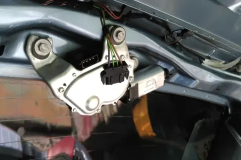 Mechanizm wycieraczki tylnej szyby, gotowy do wymiany. Widać silniczek, złącze elektryczne i mocowania.
