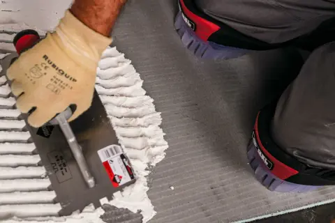 Pose d'enduit avec une truelle crantée pour le carrelage. Le choix du bon taille peigne carrelage est essentiel pour une pose parfaite.