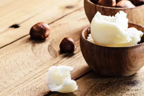Was ist Shea Butter? Cremige, weiße Shea Butter in Holzschalen, dane Nüsse. Natürliche Pflege für die Haut.