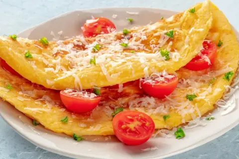 Puszysty omlet z serka wiejskiego, posypany parmezanem i udekorowany pomidorkami koktajlowymi i natką pietruszki.
