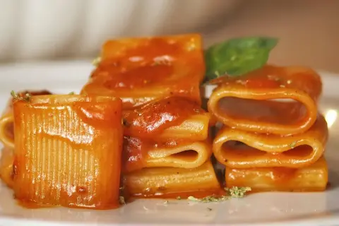 Piatto di pasta allo scarpariello, con rigatoni conditi da un sugo rosso e guarniti con basilico fresco.