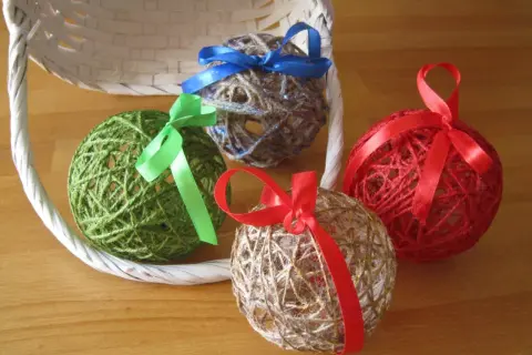 Palline decorative fatte con spago e colla vinilica, decorate con nastri colorati, appoggiate vicino a un cestino bianco.