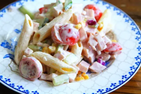 En krämig pastasallad med skinka, penne, körsbärstomater, gurka och majs. Perfekt för en snabb och god lunch.