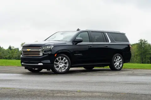 Czarny Chevrolet Suburban High Country z chromowanymi felgami stoi na mokrym parkingu, otoczony zielenią.