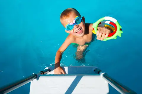Niño feliz con gafas de buceo y un juguete de agua, listo para juegos en la piscina.