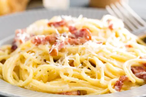 Spaghetti alla carbonara z boczkiem i parmezanem na szarym talerzu.
