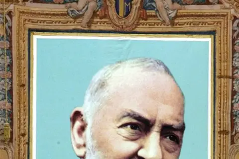 Portret Ojca Pio, jego ciało jest częściowo widoczne. Obraz ozdobiony jest bogatą ramą z motywami kwiatowymi i aniołkami.