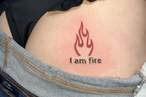 Płomień i napis "I am fire" na skórze, subtelny tatuaż na pośladku.