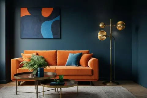 Ein orangefarbenes Sofa vor einer dunkelblauen Wand, dekoriert mit einem abstrakten Gemälde in gedeckten Farben. Ein goldener Stehlampen und zwei Couchtische ergänzen das Bild.