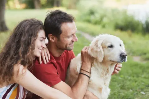 Un couple câlinant leur chien doré en plein air. Ils semblent réfléchir à comment faire garder son chien pour leurs prochaines vacances.